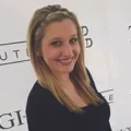 Smiling woman with long blonde hair stands in front of a white backdrop with black text.