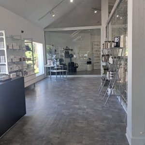 Modern salon interior with shelves of hair products, a front desk, and a large glass partition separating another room.