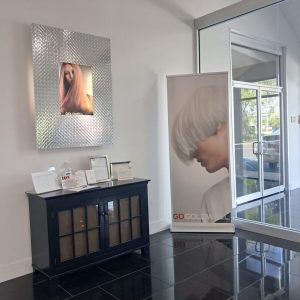 Salon lobby with a cabinet, framed photo of a woman with long hair, and a poster of a person with short, silver hair.