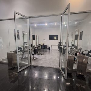 A modern hair salon with open glass doors, salon chairs, mirrors, and hairdressing equipment visible inside.