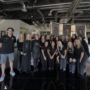 Group of people posing and smiling inside a modern salon or beauty institute with posters on the wall behind them.