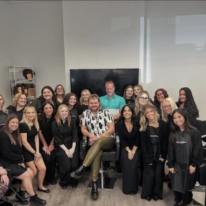 A group of people pose together in a salon, with some seated and others standing around them, all facing the camera.