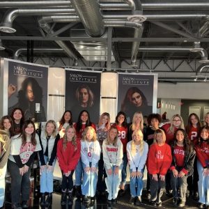 A group of women poses together inside a salon, wearing Ohio State-themed clothing and standing in front of salon posters.