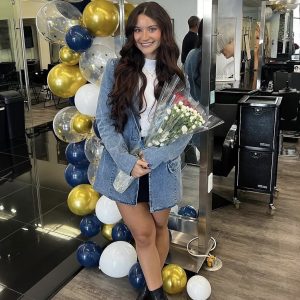 Woman holding bouquet of flowers stands in front of balloon arrangement in a modern salon.