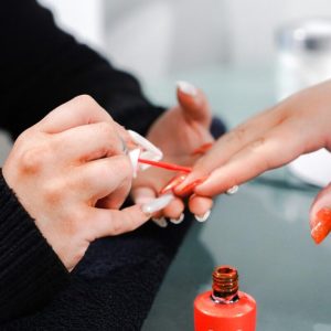 A person applies red OPI nail polish to another person's nails at a manicure station.