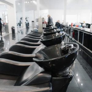 Row of black salon wash stations with sinks and chairs in a bright, modern hair salon.