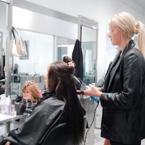 A hairstylist uses a curling iron on a seated client's hair in a modern salon.