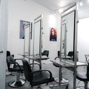 Modern hair salon with black chairs, mirrored stations, and portraits on white walls in a well-lit room.