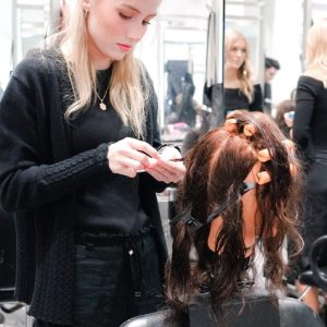 A hairstylist in a salon works on a client's hair, which is sectioned and clipped, with mirrors in the background.