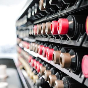 Rows of assorted coffee pods in various colors are arranged in a display rack, viewed from a side angle.
