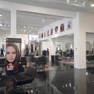 Modern hair salon interior with empty black chairs, large mirrors, and portraits of models displayed on the walls.