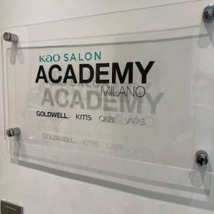 A clear sign on a wall reads "KAO Salon Academy Milano" with the brands Goldwell, KMS, Oribe, and Varis listed below.